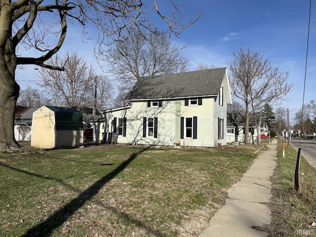 view of front of property featuring a storage unit, an outbuilding, a front lawn, and a shingled roof