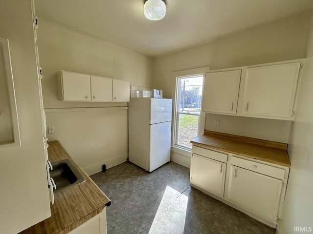 kitchen featuring white cabinets, butcher block counters, and freestanding refrigerator