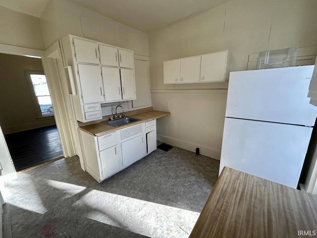 kitchen featuring white cabinets, freestanding refrigerator, baseboards, and a sink