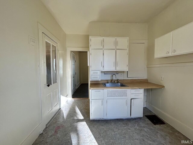 kitchen featuring a sink, baseboards, light countertops, and white cabinetry