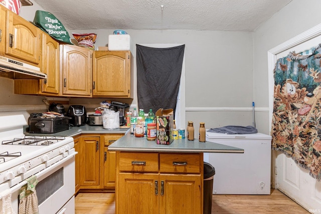 kitchen featuring under cabinet range hood, light wood-type flooring, a textured ceiling, and white gas range oven