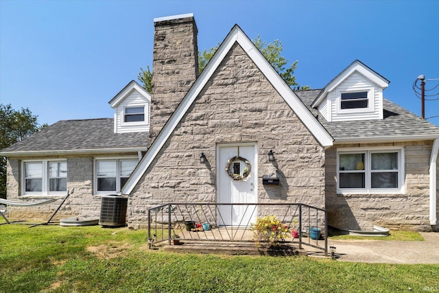 view of front of home with central air condition unit, a chimney, a front yard, and a shingled roof