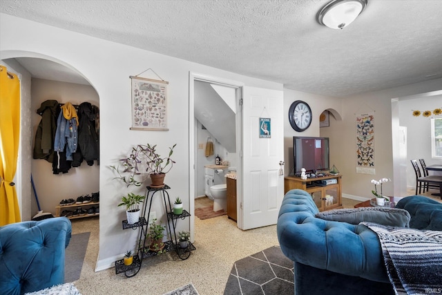 living room with arched walkways, a textured ceiling, speckled floor, and baseboards