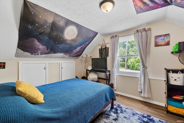 bedroom with baseboards, lofted ceiling, a textured ceiling, and wood finished floors
