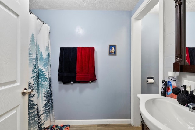 full bathroom featuring a sink, baseboards, a textured ceiling, and wood finished floors