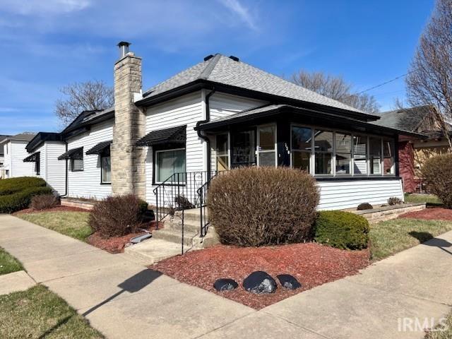 view of front of property featuring a chimney, roof with shingles, and a sunroom