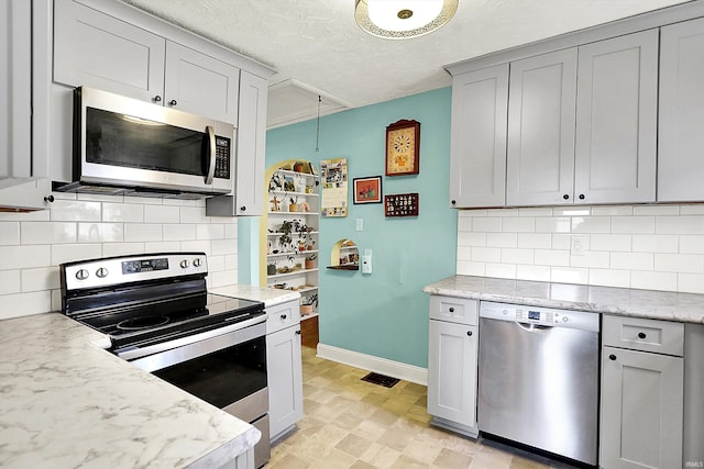 kitchen featuring appliances with stainless steel finishes, gray cabinetry, baseboards, visible vents, and decorative backsplash