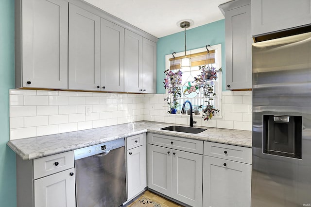 kitchen featuring tasteful backsplash, a sink, light stone counters, pendant lighting, and appliances with stainless steel finishes