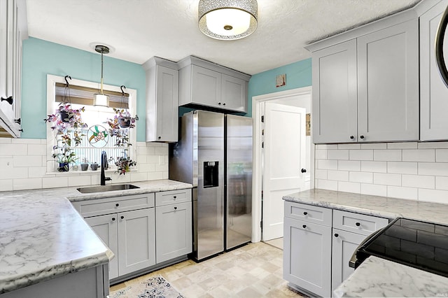 kitchen with stainless steel fridge with ice dispenser, range, hanging light fixtures, a sink, and light stone counters