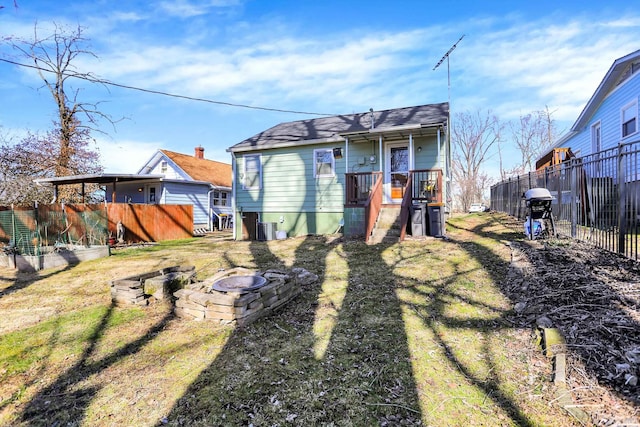 rear view of property featuring an outdoor fire pit, a yard, central AC, and fence