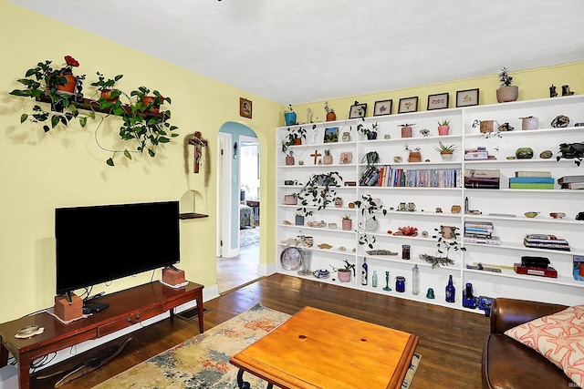 living area featuring arched walkways, baseboards, and wood finished floors