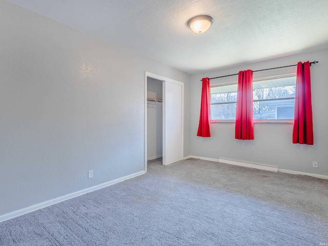 unfurnished bedroom featuring a closet, baseboards, a textured ceiling, carpet flooring, and a baseboard heating unit