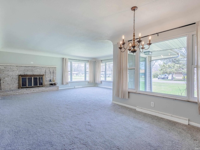unfurnished living room featuring baseboard heating, a notable chandelier, a glass covered fireplace, and carpet floors