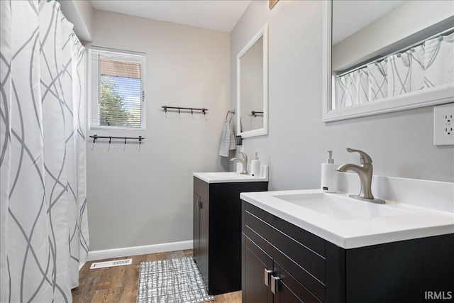 bathroom with baseboards, wood finished floors, a sink, and two vanities