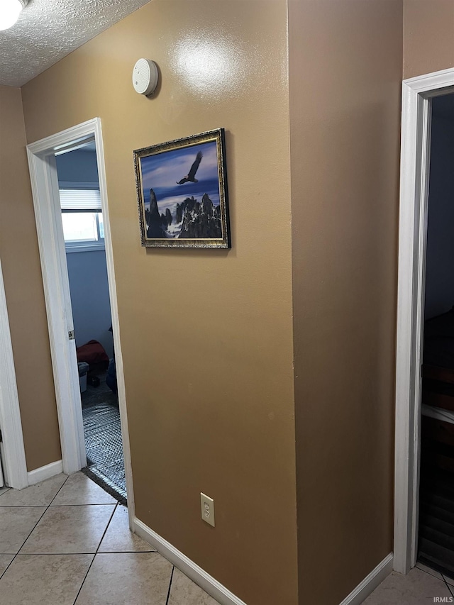 hallway with light tile patterned flooring, baseboards, and a textured ceiling