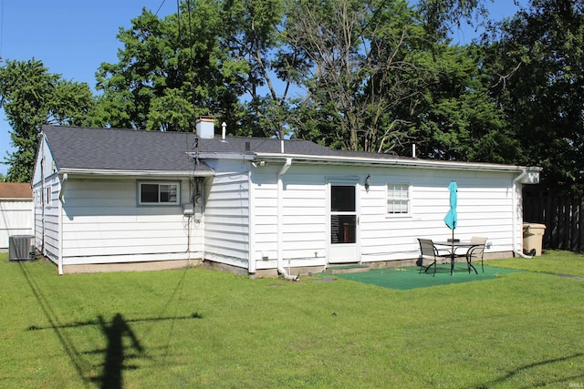 back of house with central air condition unit, a chimney, fence, a shingled roof, and a yard