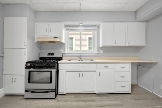 kitchen featuring under cabinet range hood, stainless steel gas range oven, a sink, and white cabinets