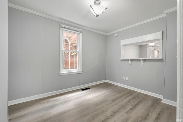 spare room with baseboards, visible vents, wood finished floors, and ornamental molding