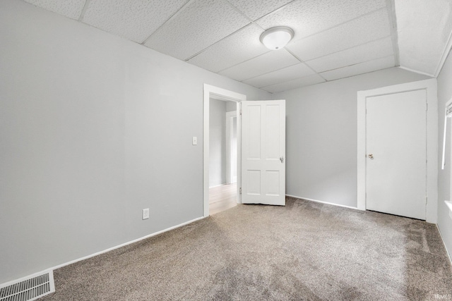 empty room with carpet flooring, visible vents, and a drop ceiling