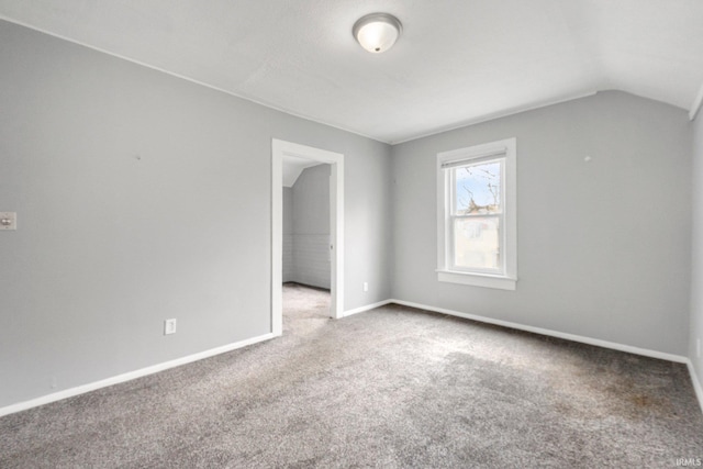 carpeted spare room with baseboards and vaulted ceiling