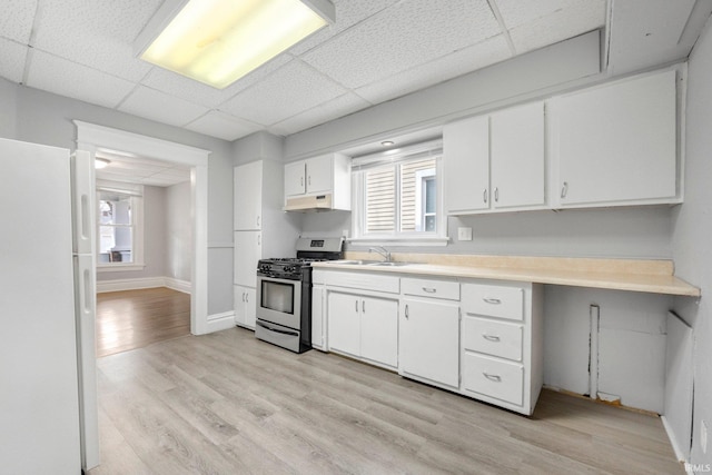 kitchen featuring stainless steel range with gas cooktop, under cabinet range hood, a sink, freestanding refrigerator, and light wood-style flooring