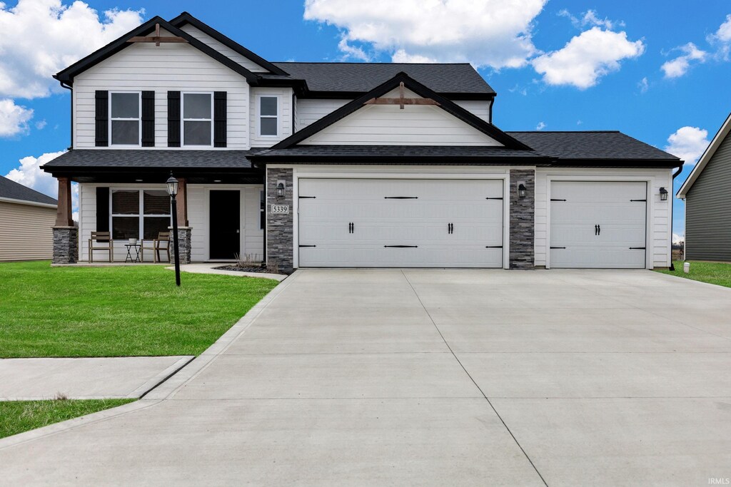 view of front of home with stone siding, an attached garage, a front yard, driveway, and a porch