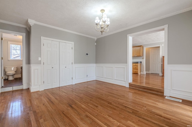 unfurnished dining area with a textured ceiling, visible vents, wood finished floors, an inviting chandelier, and wainscoting