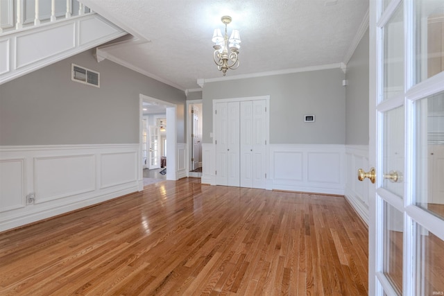 spare room featuring light wood-type flooring, a textured ceiling, a chandelier, and visible vents