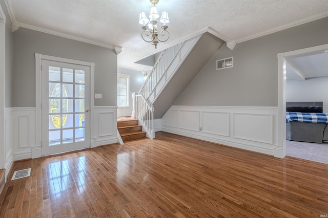 additional living space with stairway, an inviting chandelier, wood-type flooring, a textured ceiling, and visible vents