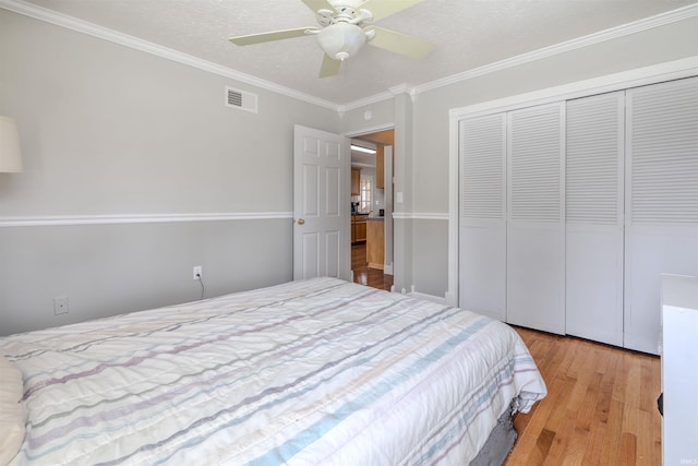 bedroom with a closet, visible vents, crown molding, wood finished floors, and a ceiling fan