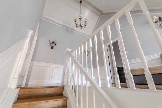 staircase featuring a wainscoted wall, high vaulted ceiling, a decorative wall, and a chandelier
