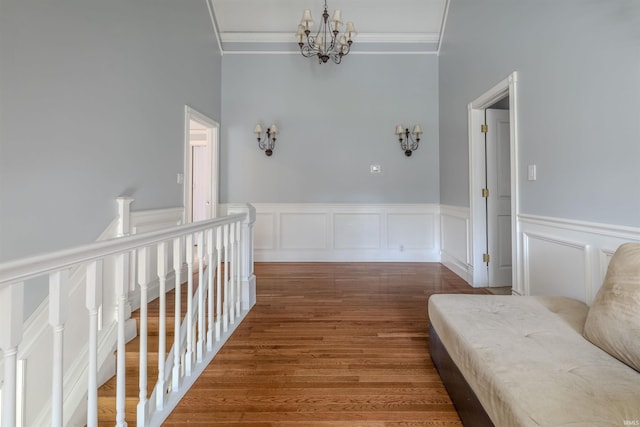 hall featuring a wainscoted wall, an upstairs landing, ornamental molding, wood finished floors, and an inviting chandelier