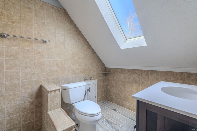 bathroom with tile walls, toilet, lofted ceiling with skylight, and vanity