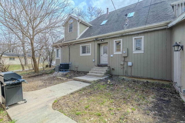 rear view of house with central AC unit, roof with shingles, and entry steps