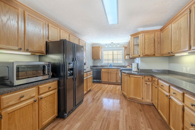 kitchen with a textured ceiling, glass insert cabinets, a sink, light wood-type flooring, and black appliances