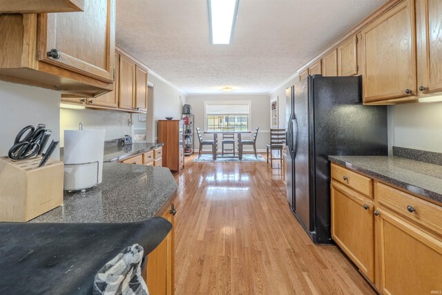 kitchen with black fridge with ice dispenser, crown molding, a textured ceiling, dark stone counters, and light wood finished floors