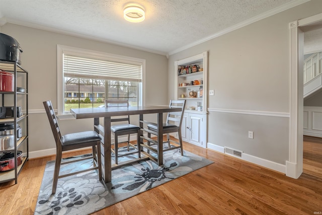 dining room featuring a textured ceiling, ornamental molding, visible vents, and wood finished floors