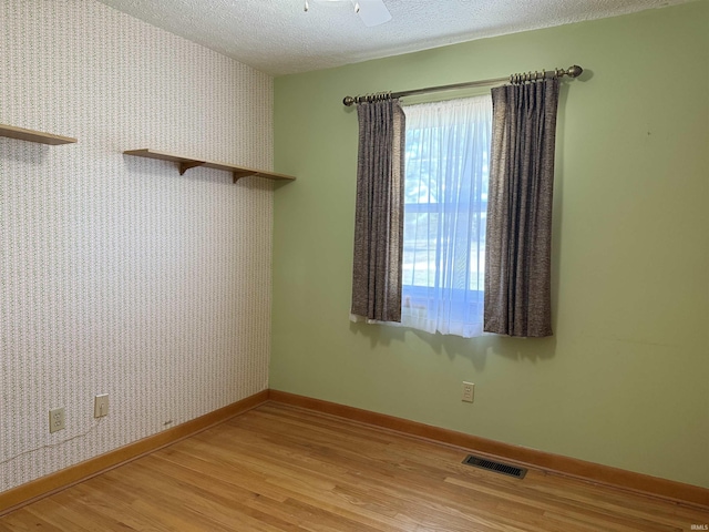 spare room with a textured ceiling, light wood-style flooring, visible vents, and wallpapered walls