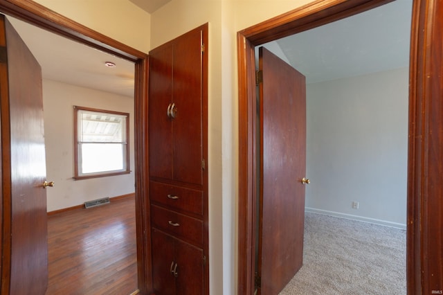 hall with baseboards, carpet floors, visible vents, and wood finished floors