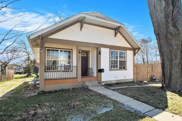 bungalow-style house with a front lawn, covered porch, and fence