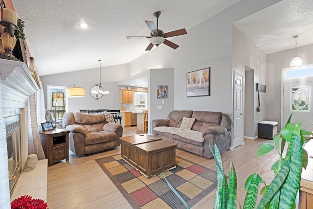 living room with light wood-style flooring, vaulted ceiling, a fireplace, and a textured ceiling