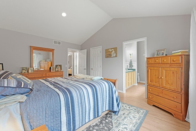 bedroom featuring connected bathroom, visible vents, light wood-style floors, and lofted ceiling