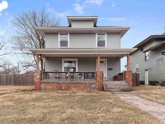 american foursquare style home featuring a porch, fence, and a front lawn
