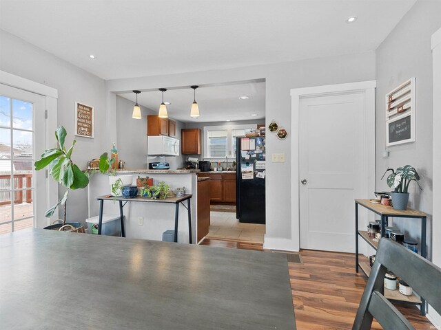 kitchen featuring a peninsula, light wood finished floors, white microwave, brown cabinetry, and freestanding refrigerator