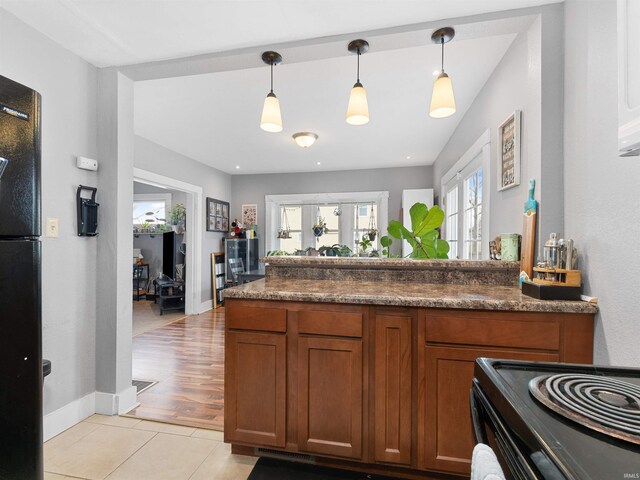 kitchen featuring hanging light fixtures, brown cabinetry, light tile patterned floors, dark countertops, and black appliances