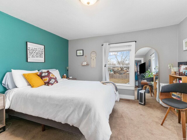 bedroom with light carpet, baseboards, and arched walkways