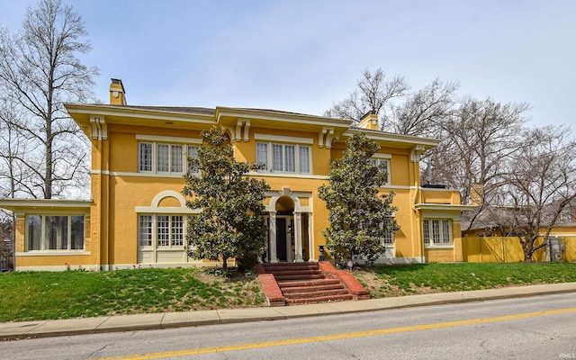 italianate home featuring a chimney, stucco siding, a front lawn, and fence