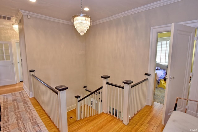corridor featuring ornamental molding, an upstairs landing, an inviting chandelier, and wood finished floors