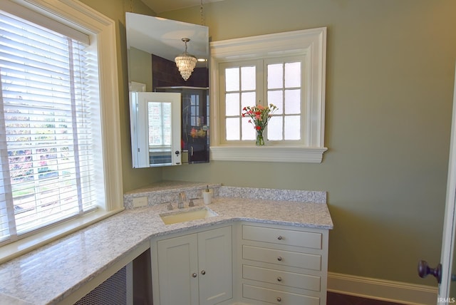 kitchen with a sink, baseboards, white cabinetry, light stone countertops, and a notable chandelier