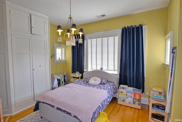 bedroom with an inviting chandelier, visible vents, and light wood-style floors